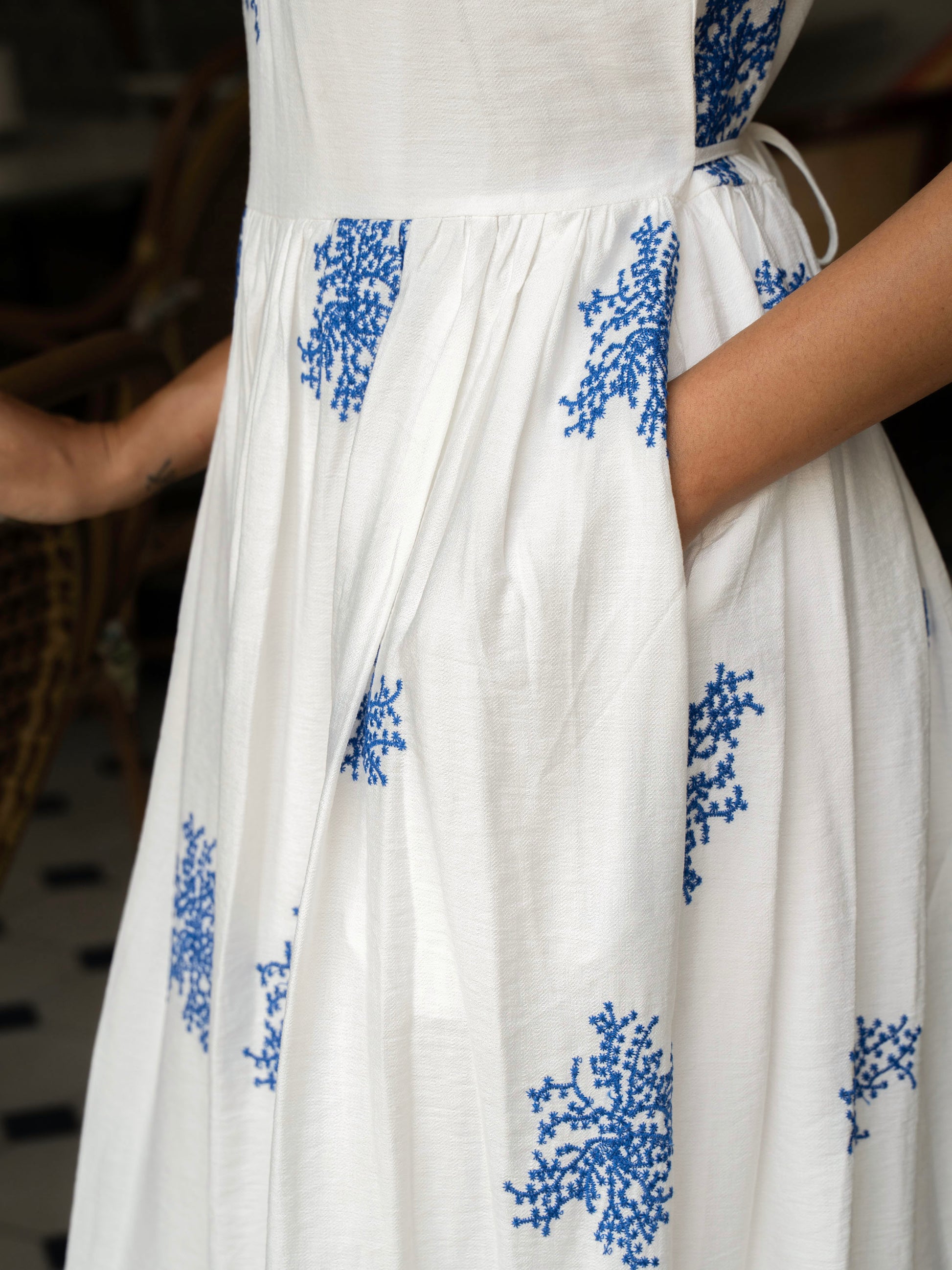 Side close up view of model- her hand in the pocket of Embroidered sleeveless maxi in cotton-silk with halter neck, tie-back waist, and pockets-MISSVI